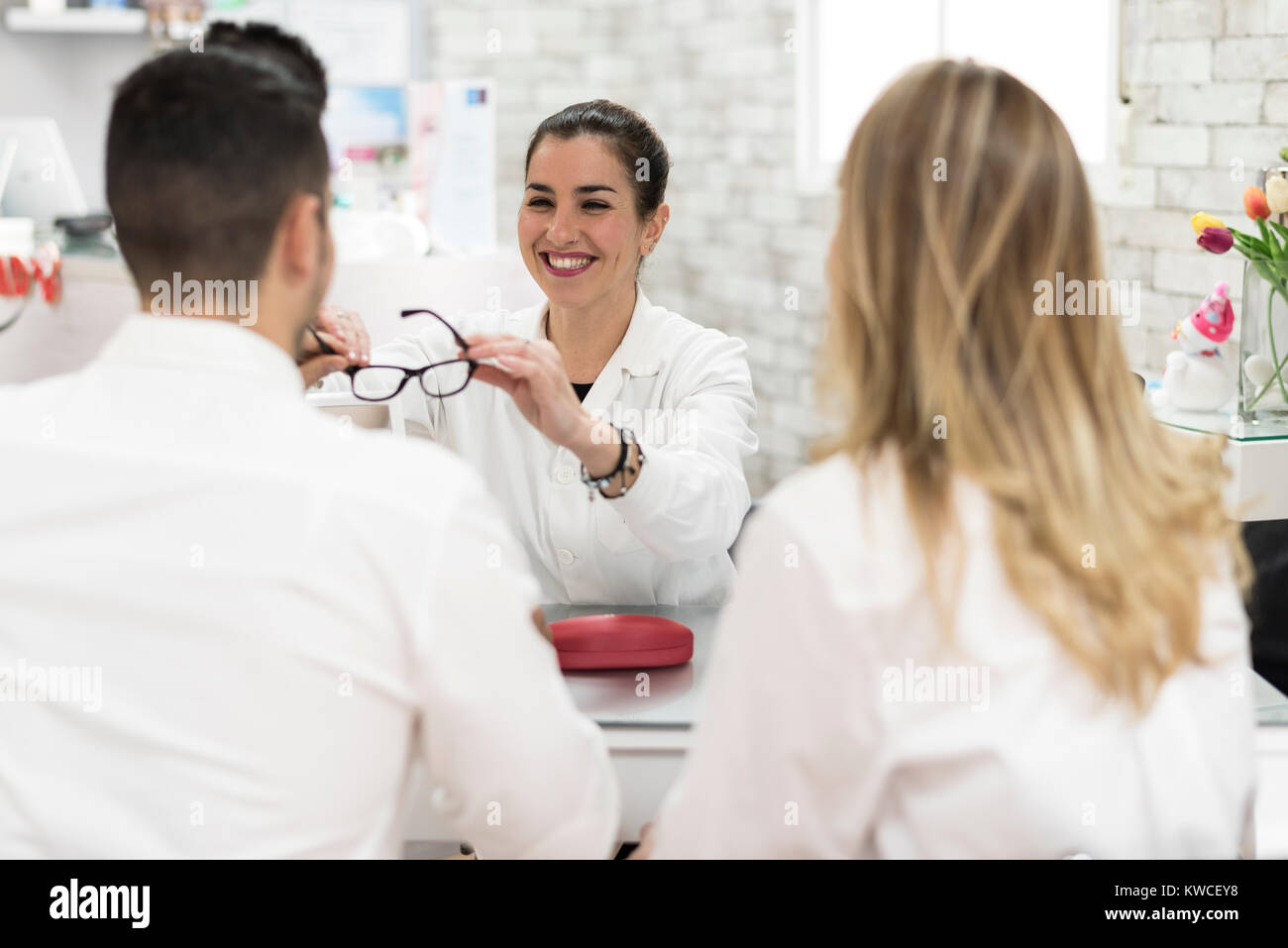 Joven oculista mujer vendiendo gafas para pareja en tienda Foto de stock