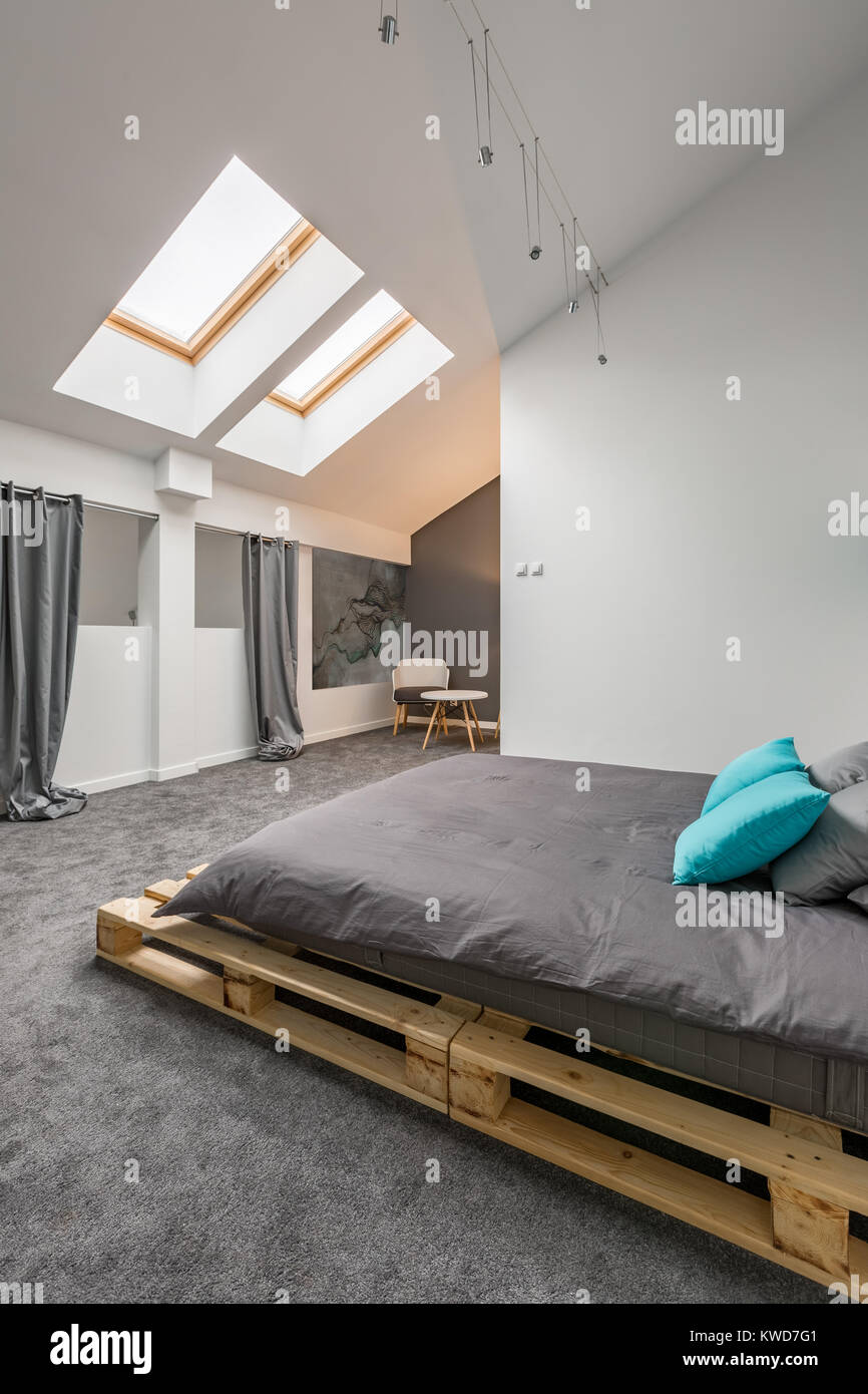 Habitación abuhardillada con cama de palet y suelo gris Fotografía de stock  - Alamy