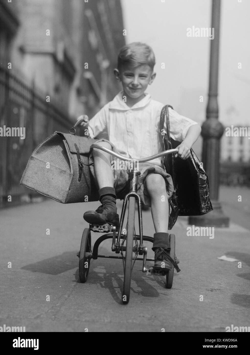 Joven monta su triciclo en las aceras de la ciudad de Nueva York, c. 1920. Él es transportar dos paquetes de la tienda de comestibles local (BSLOC 2016 8 85) Foto de stock