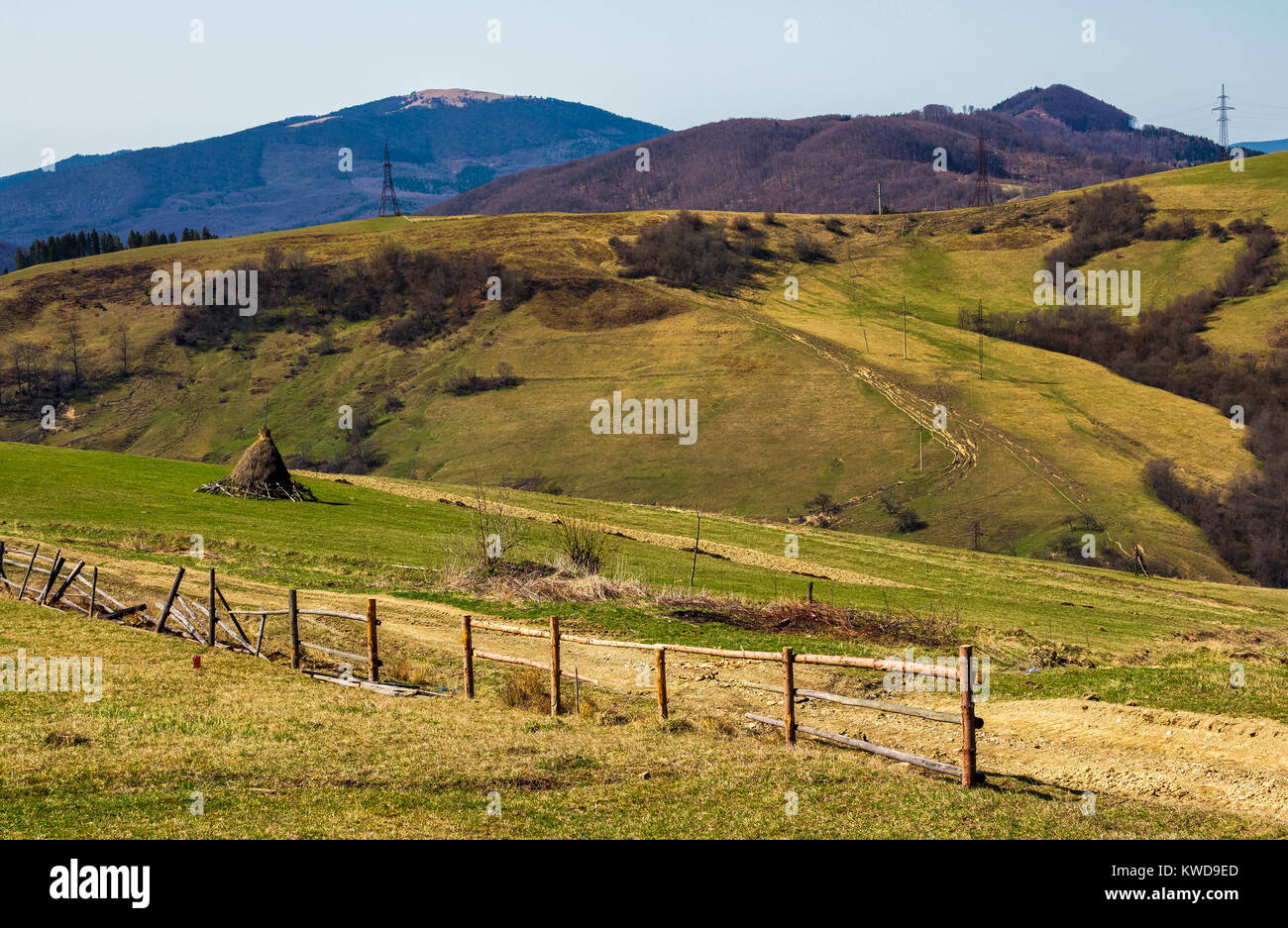 Zona rural en colinas en primavera. valla de madera y pajar, cerca de la carretera. un montón de postes de electricidad Foto de stock