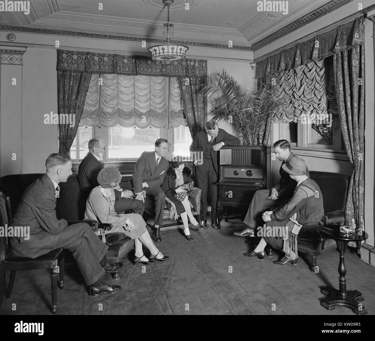 Grupo de hombres y mujeres escuchando una radio en el Hotel Hamilton, Washington, D.C., el Atwater Kent radio incorpora un altavoz cerrado en la parte superior del armario. La foto se asoció con Thomas R. Shipp es trabajo de relaciones públicas para Atwater Kent Radios (BSLOC_2016_10_57) Foto de stock