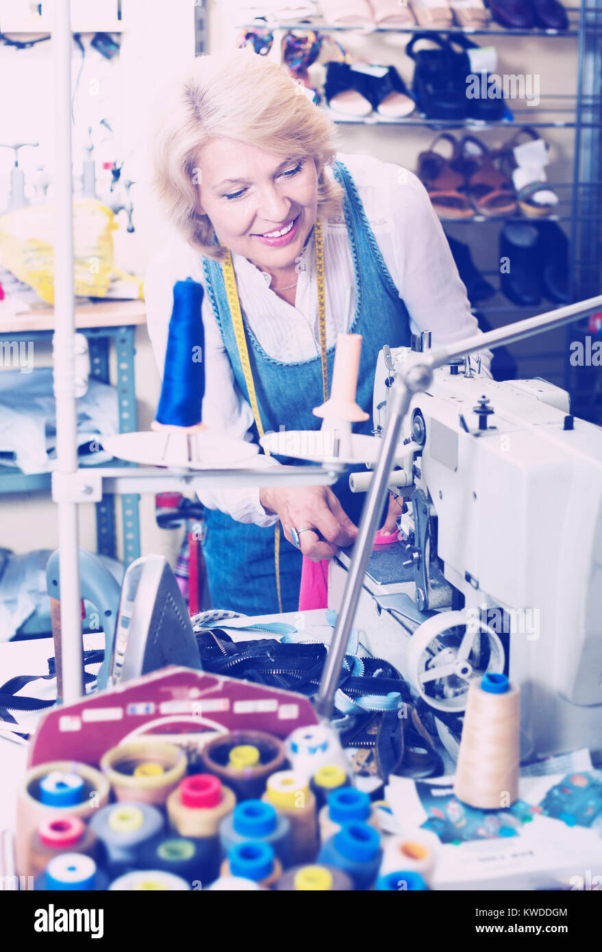 Alegre hembra madura adaptar mediante máquina de coser en el taller Foto de stock