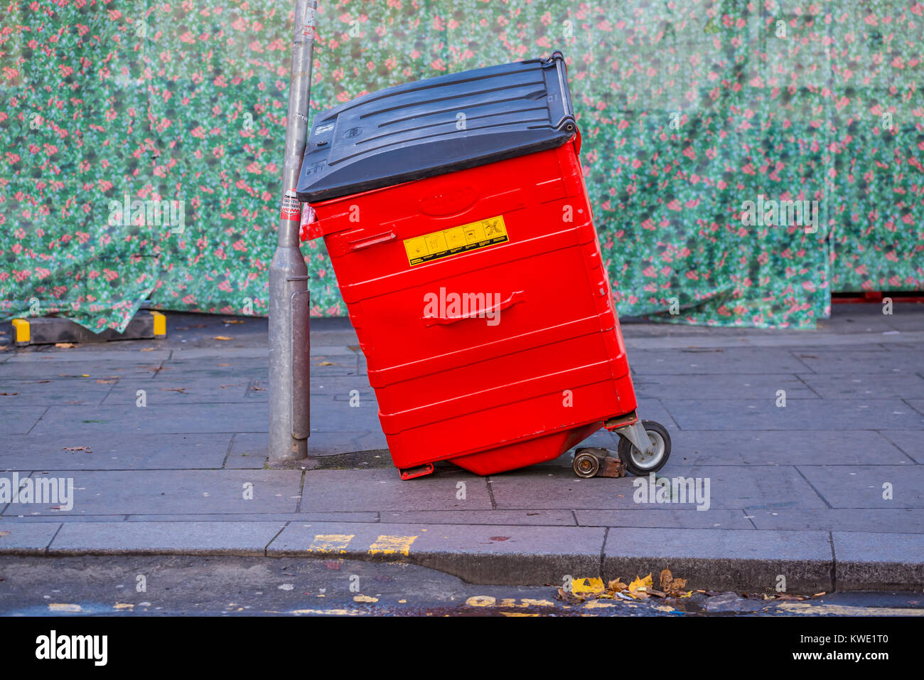 Cubo de basura roto apoyado por un semáforo en una calle de la ciudad, Reino Unido Foto de stock