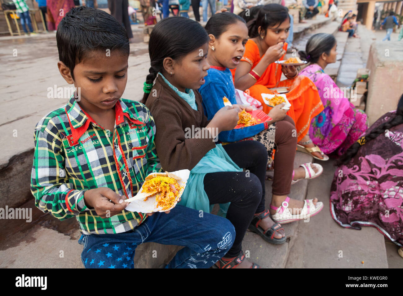 Los niños comen un bocadillo de bhel puri en los ghats de Varanasi en India Foto de stock
