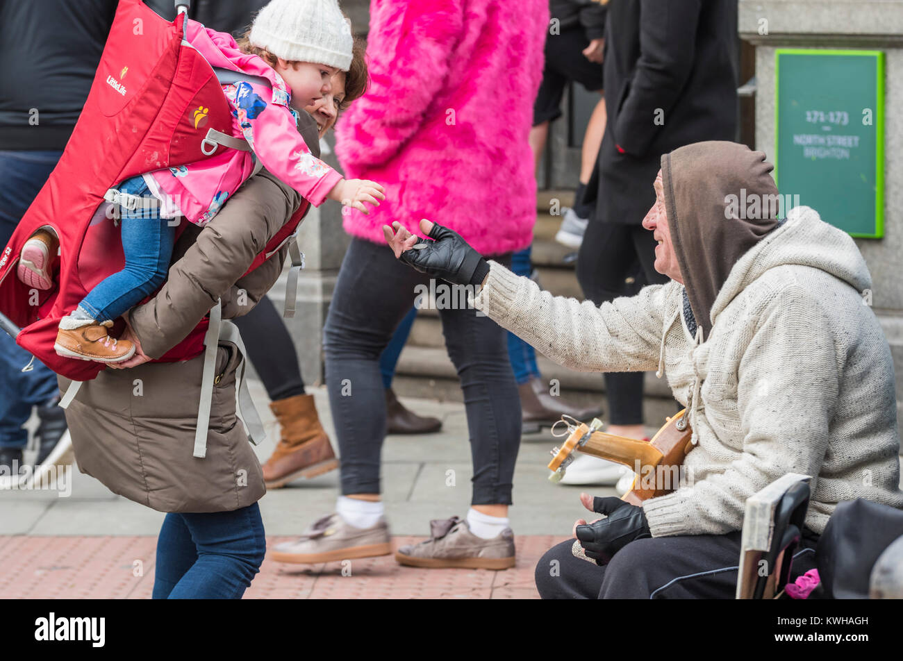 Niños pequeños sobre los hombros de las mujeres dando dinero a un músico callejero de calle en el Reino Unido. Folleto Foto de stock