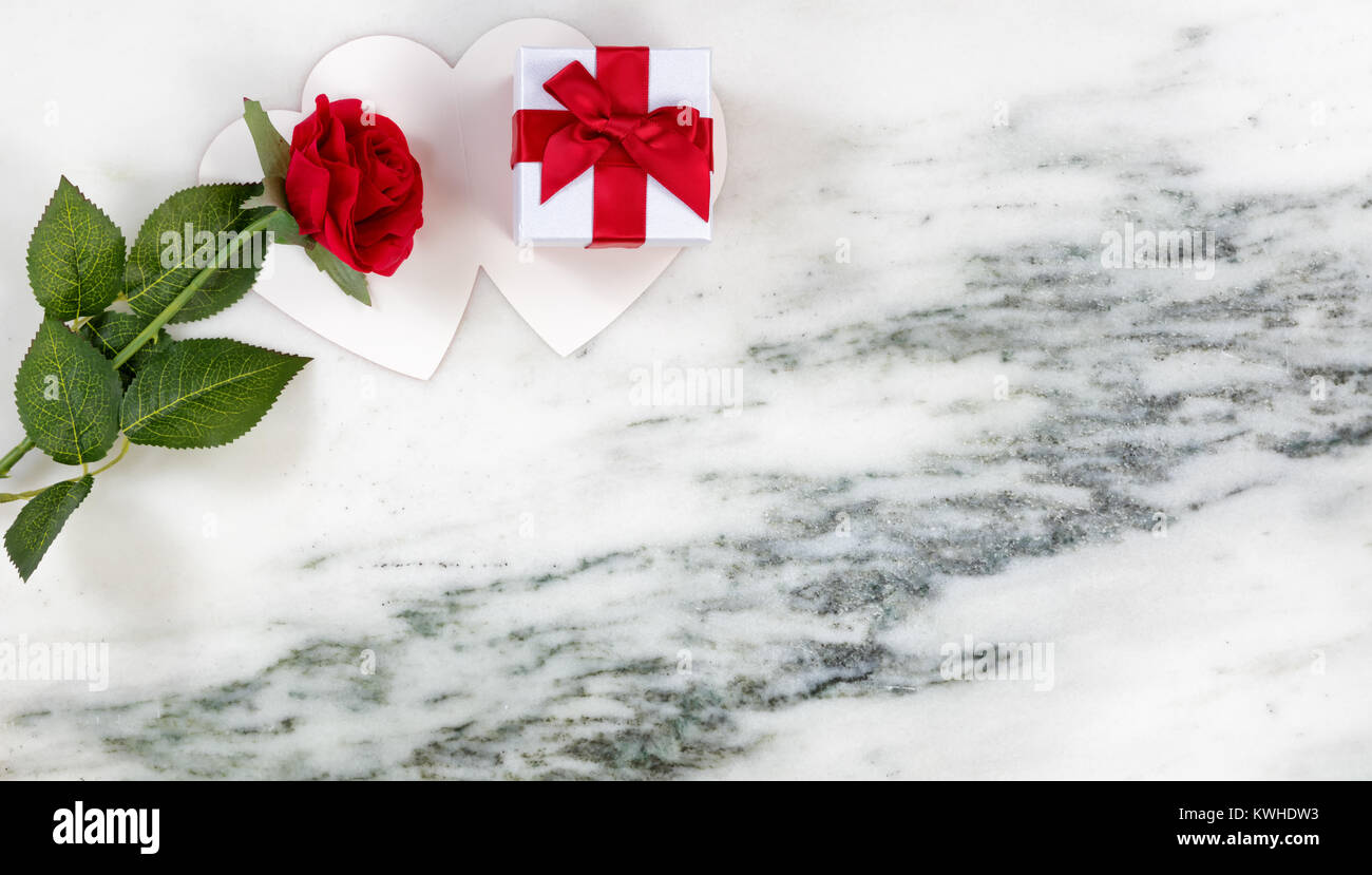 Descansando sobre una rosa roja y caja de regalo tarjeta sobre fondo de piedra de mármol en plana vista laicos Foto de stock