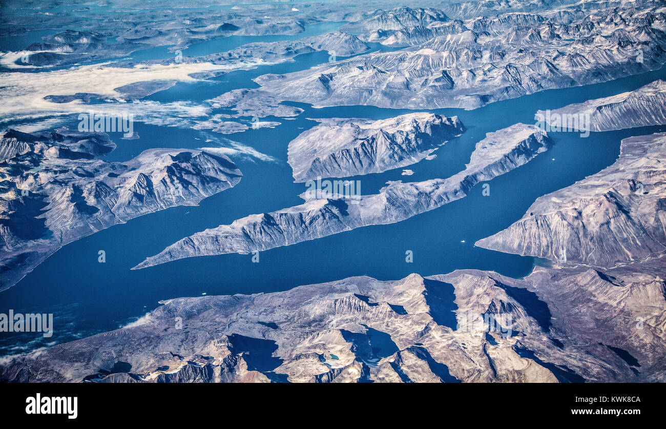 Vistas panorámicas aéreas de escarpado paisaje de Groenlandia mostrando los glaciares, icebergs y montañas en un hermoso día soleado con el cielo azul y las nubes Foto de stock