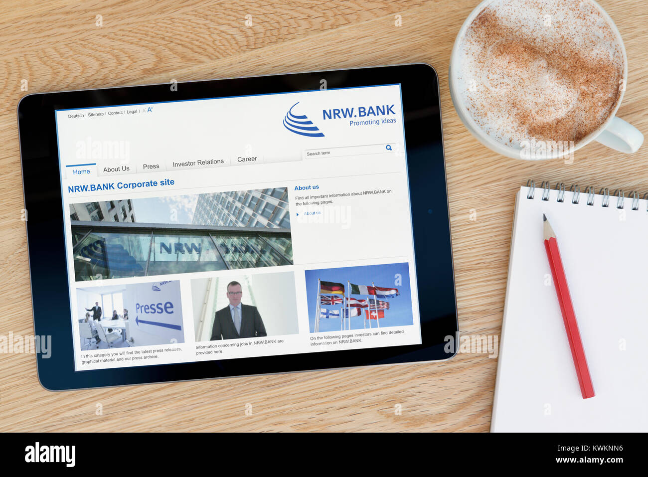 El NRW.BANK web sobre un dispositivo tablet iPad, descansando sobre una mesa de madera junto a un bloc de notas, lápiz y la taza de café (Editorial) Foto de stock