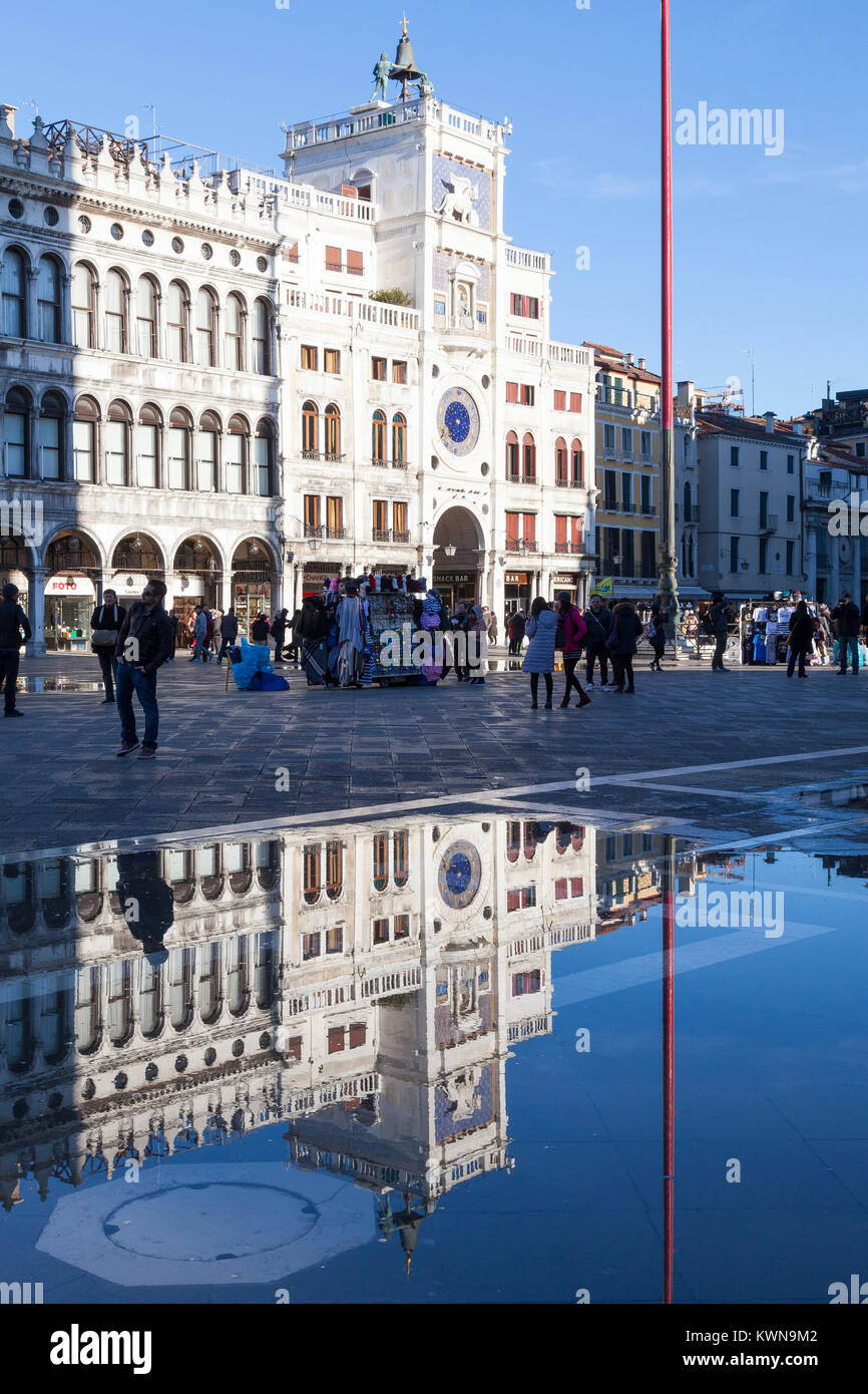 La Torre del Reloj, la Piazza San Marco, Venecia, Italia iluminada por un eje de sol de invierno se refleja en acqua alta marea alta Foto de stock