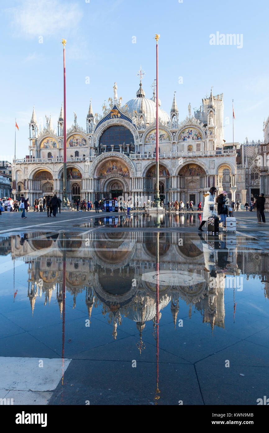 La Basílica de San Marcos se refleja en acqua alta en Piazza San Marco con turistas, wheeling maletas Venecia, Véneto, Italia Foto de stock