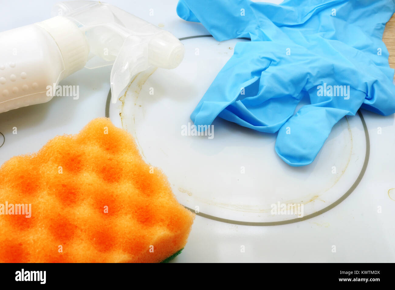 Limpieza sucia encimera eléctrica. Cerca de guante azul, el polvo y la esponja en la estufa blanca. Foto de stock