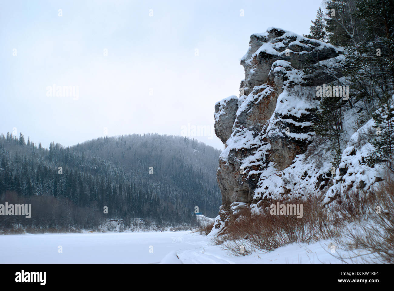 Una pintoresca roca en la orilla de un estanque congelado de invierno en las montañas boscosas Foto de stock