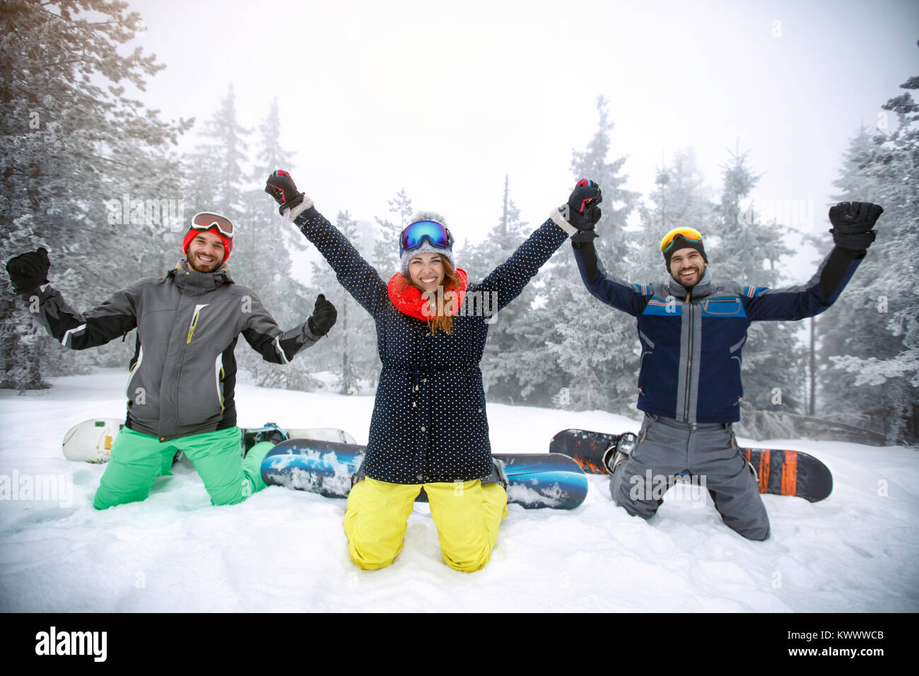 Hembra con dos machos snowboarders arrodillado sobre la nieve con manos levantadas Foto de stock