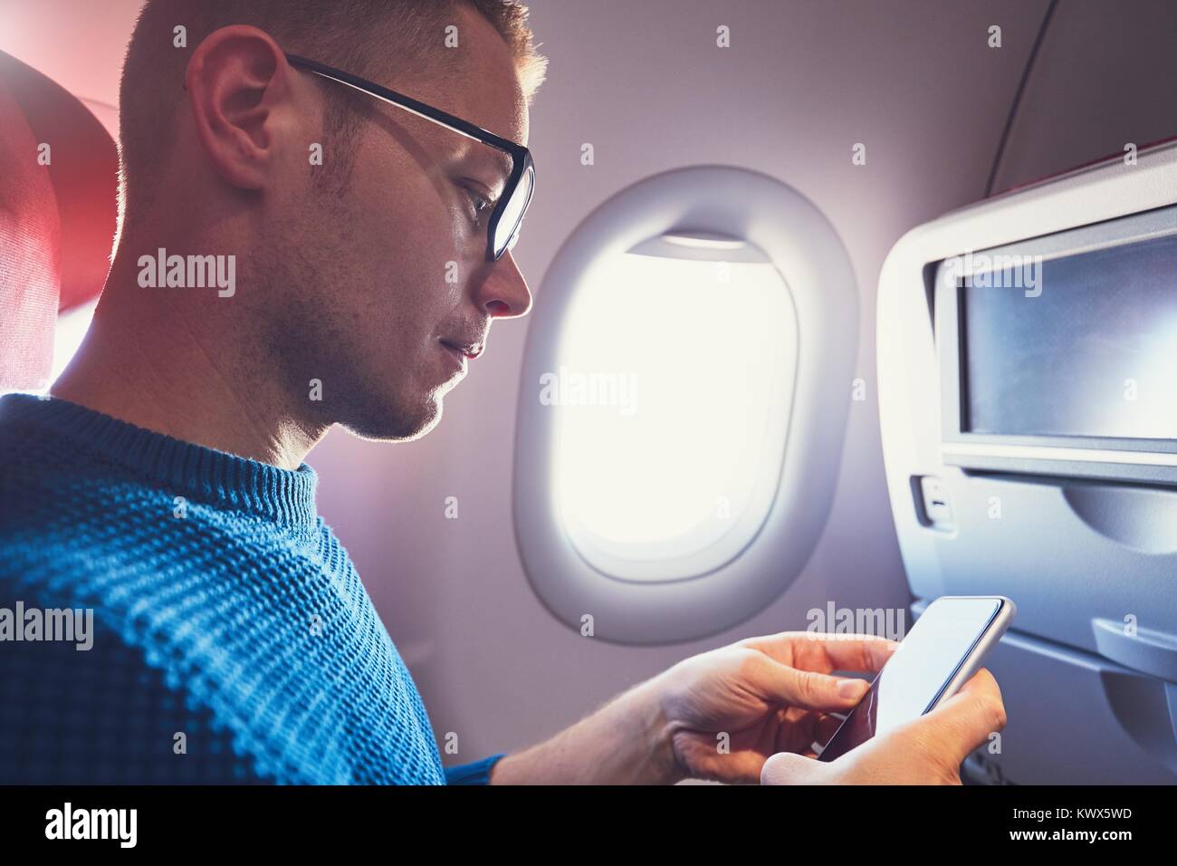 Conexión en el avión. Joven viajero (pasajero) utilizando el teléfono inteligente durante el vuelo. Foto de stock