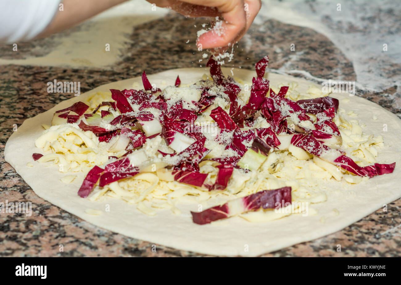 Raw original italiana fresca pizza, pasta preparación en estilo tradicional: el chef distribuye el queso y RABANO ROJO . Comida, cocina italiana y C Foto de stock