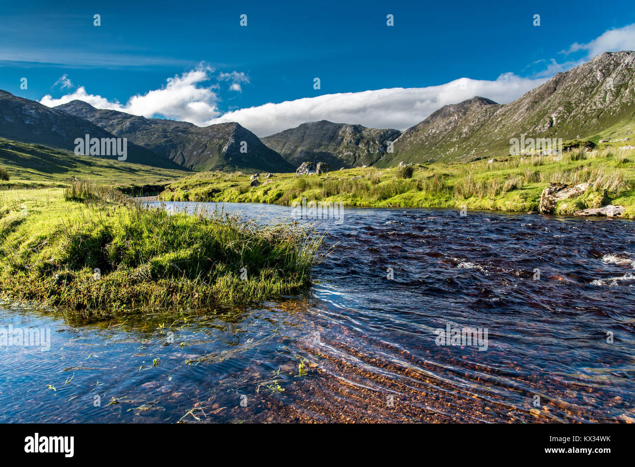 Paisaje de Connemara en Irlanda: Un río fluye en medio de los prados en la parte delantera de las majestuosas Montañas Twelve Bens Foto de stock