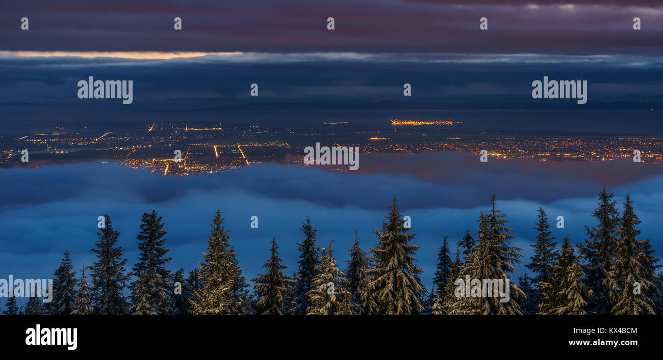 Vista de la ciudad desde la cima de la montaña en invierno sobre las nubes en la noche. Foto de stock