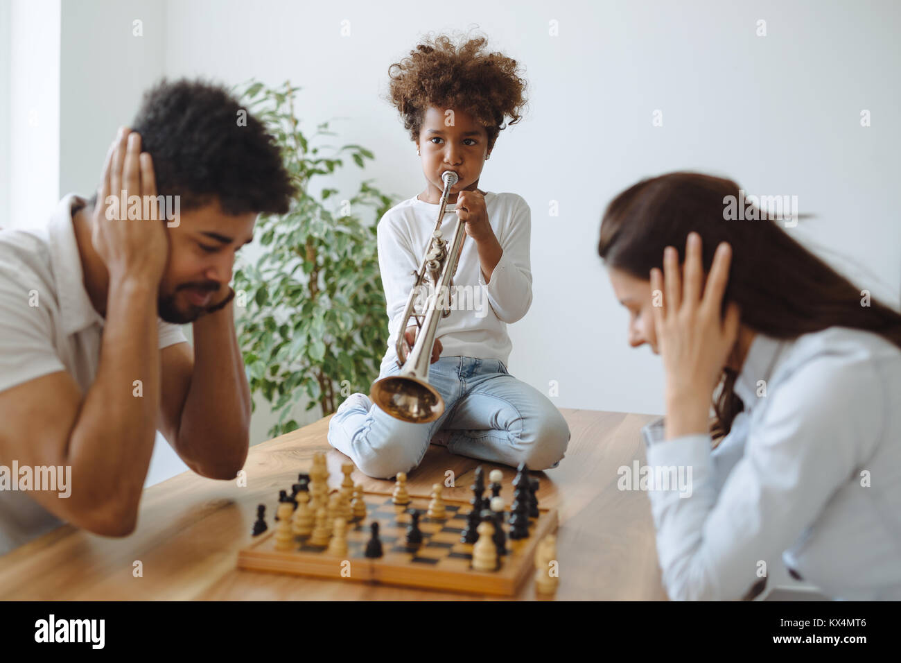 La madre y el padre tratando de jugar al ajedrez, mientras su hijo juega trompeta Foto de stock
