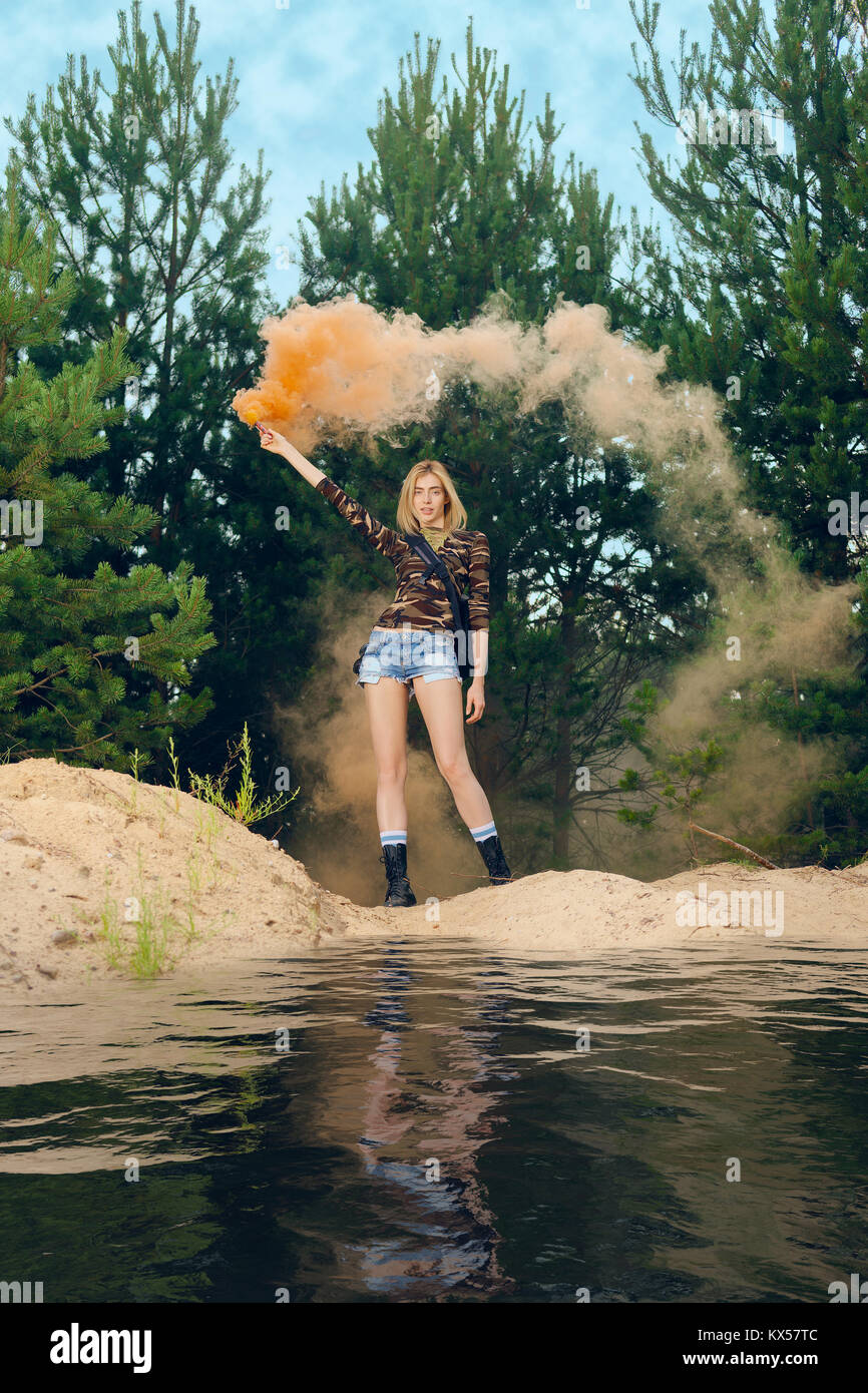 Excursionista perdido menea el humo bengala a señal para ayudar en la parte exterior de la madera en pie por el lago Foto de stock