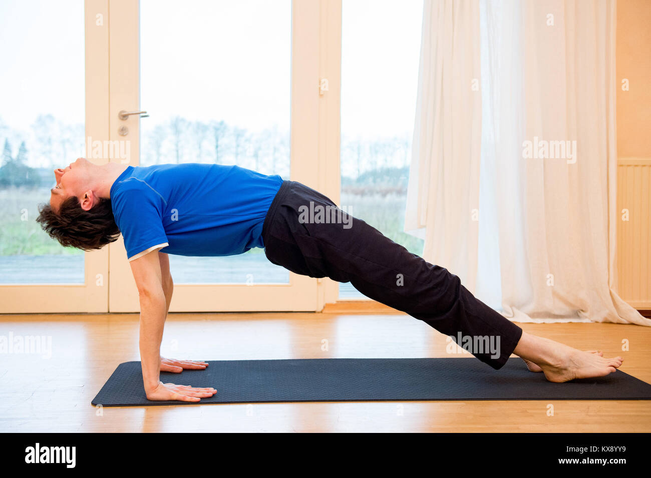 El hombre practicando yoga en interiores, en un espacio de retiro haciendo la postura de la tabla - Purvottanasana ascendente Foto de stock