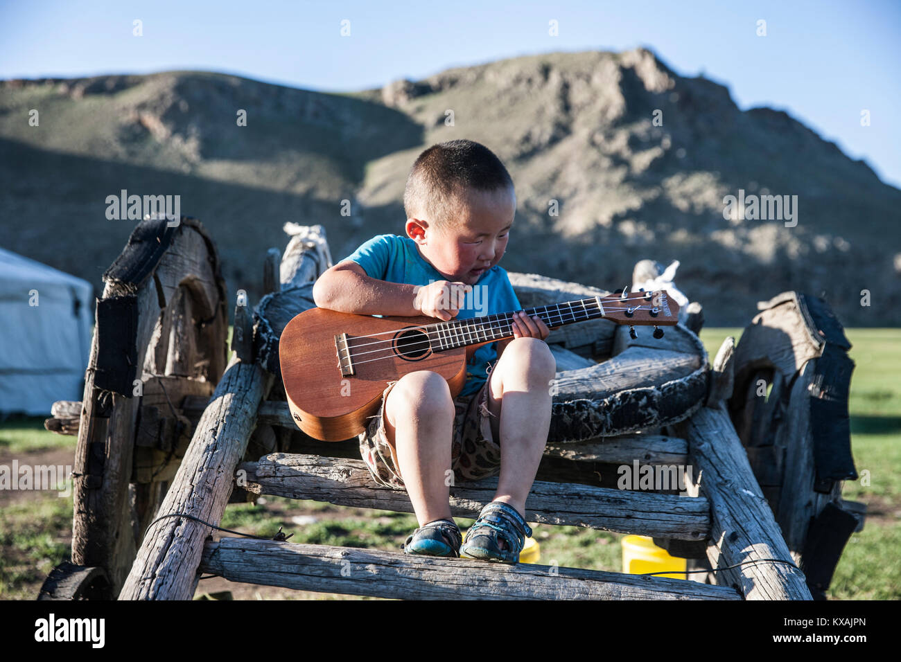 Niño mongol tocando la guitarra mientras están sentados en el carro, Bunkhan yak, Bulgan, Mongolia Foto de stock