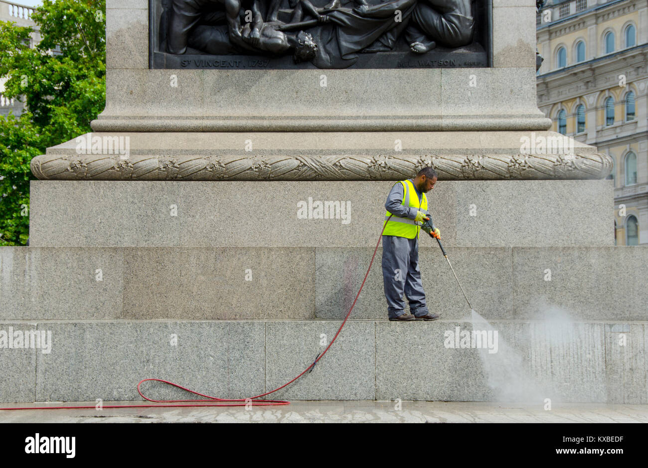 Londres, Inglaterra, Reino Unido. El hombre la limpieza de la base de la columna de Nelson, con una arandela de presión Foto de stock