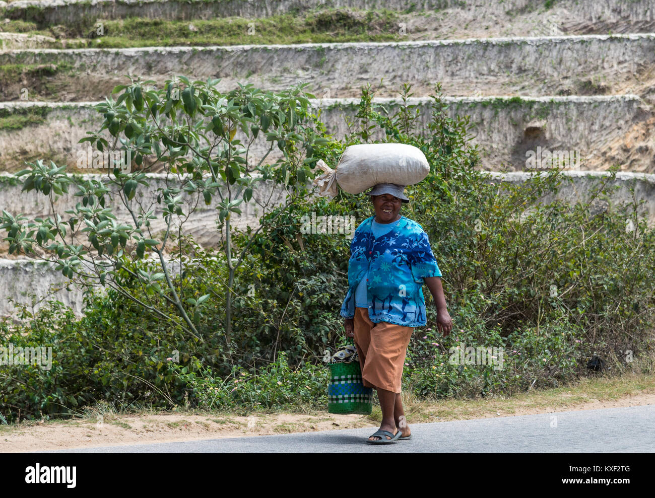 Una mujer local con una gran sonrisa llevando un saco sobre su cabeza. Madagascar, África. Foto de stock