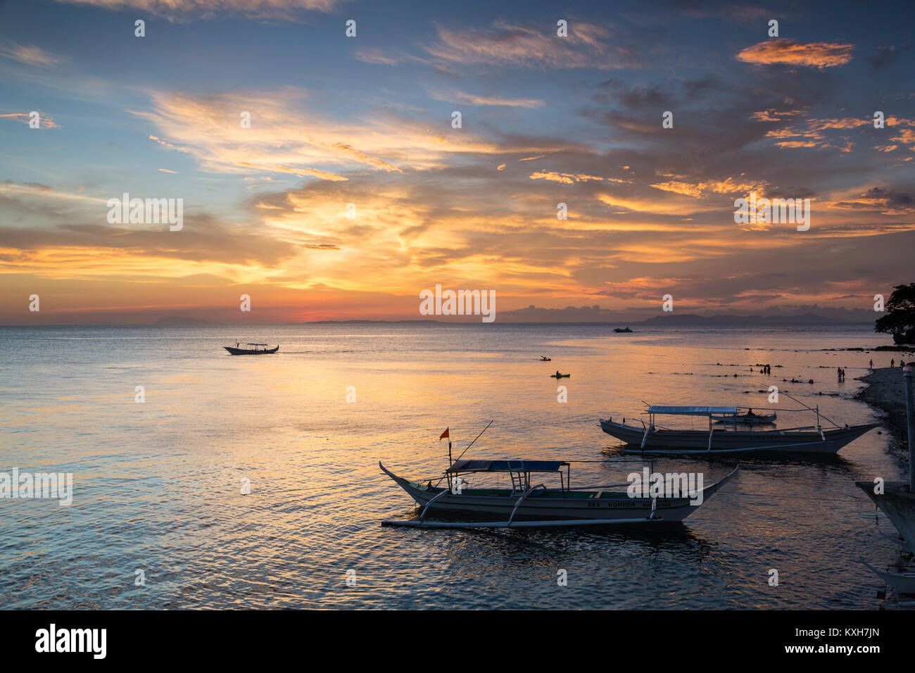 Bangka barcas reposan sobre el litoral bajo un vibrante sunset sky en Anilao, Filipinas. Foto de stock