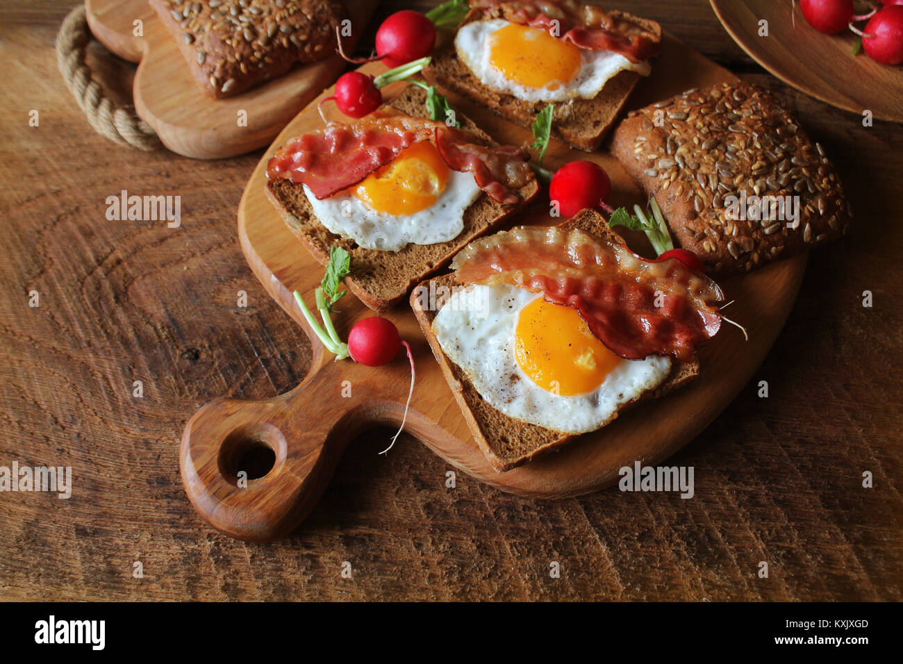 Desayuno de crujiente de bacon, huevos fritos y pan. Sándwiches en la tabla de cortar. Tabla rústica Foto de stock