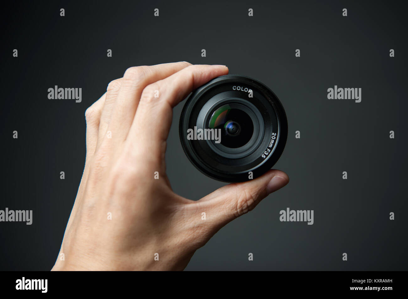 Mano de hombre sosteniendo un lente de la cámara sobre un fondo negro Foto de stock