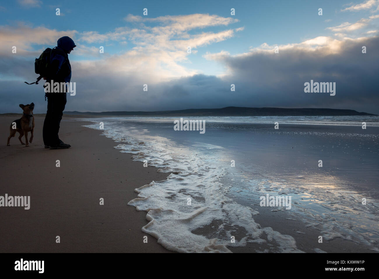 Hombre caminando perro en el Strand playa grande en la hermosa luz del atardecer en invierno, en la Isla de Islay, Escocia Foto de stock