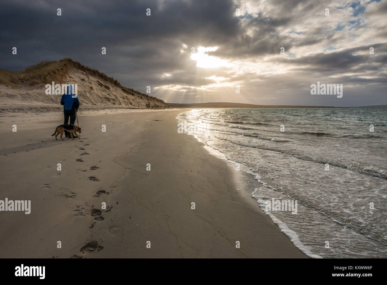 Iluminado por las dunas de arena en la playa en Loch Gruinart Killinallan dramáticos de invierno bajo la luz solar con walker persona y perro, la Isla de Islay, Escocia Foto de stock