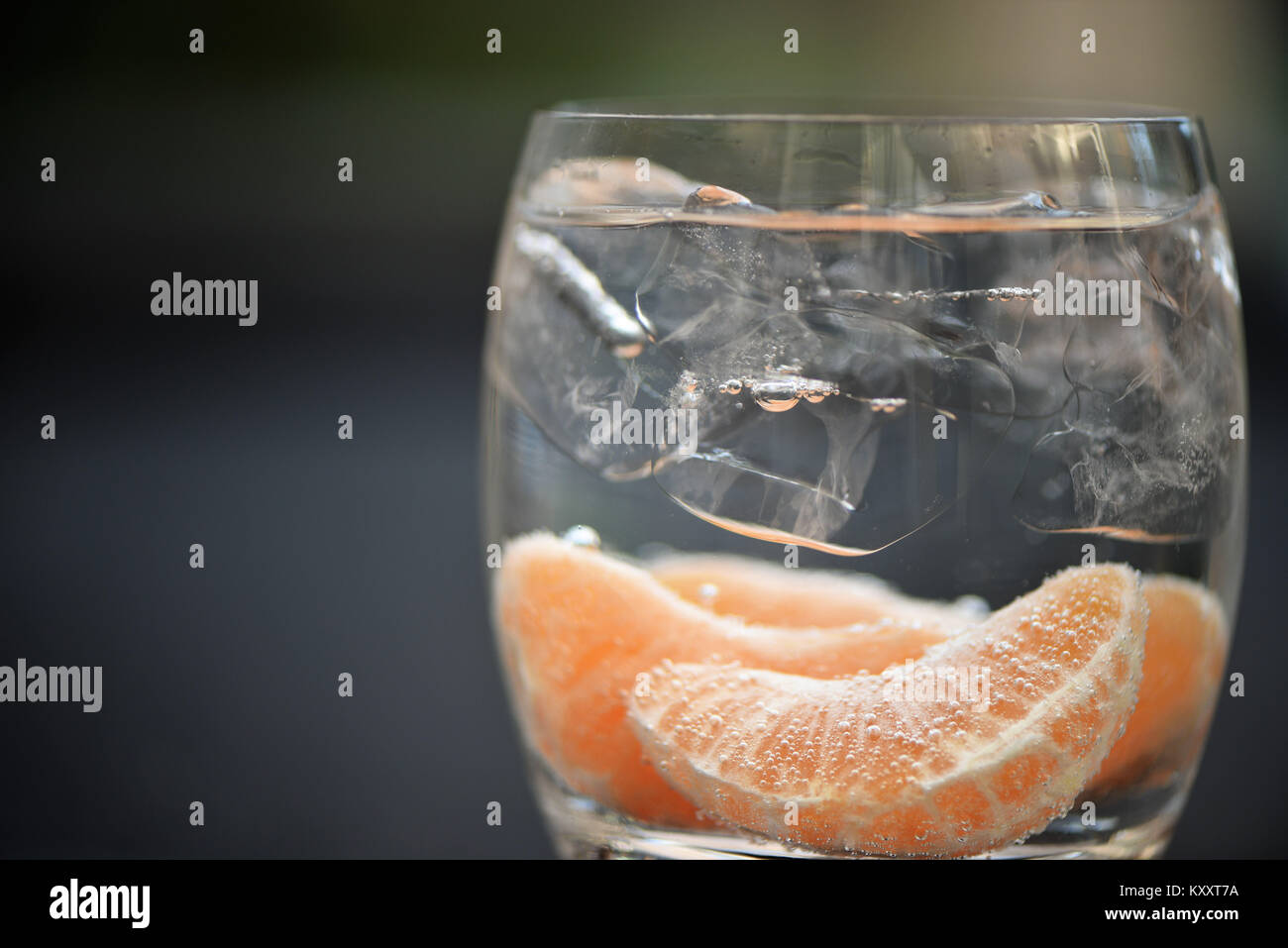 Comida y bebida la fotografía macro imagen saludable de frutas de naranja en un vaso de agua gasificada con burbujas y cubitos de hielo con fondo desenfocado y espacio Foto de stock