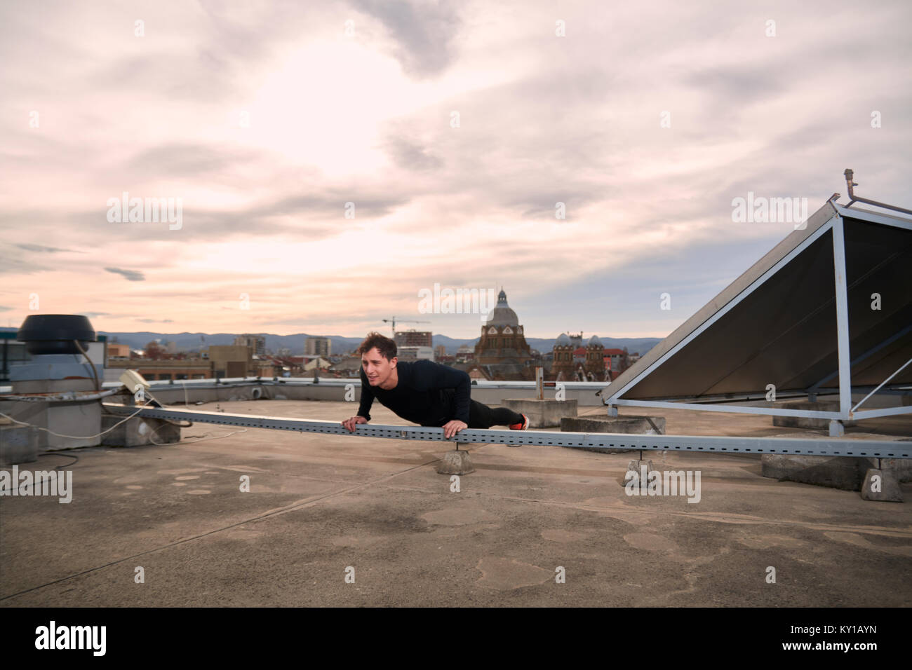 Un hombre joven, de ejercicios al aire libre en la azotea, centro urbano de techos, azoteas detrás, paisaje urbano Foto de stock
