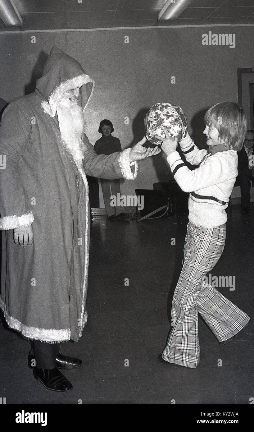 1970, históricos, excitado joven vistiendo pantalones estampados comprobación quemado recibir un regalo de Papá Noel. Foto de stock