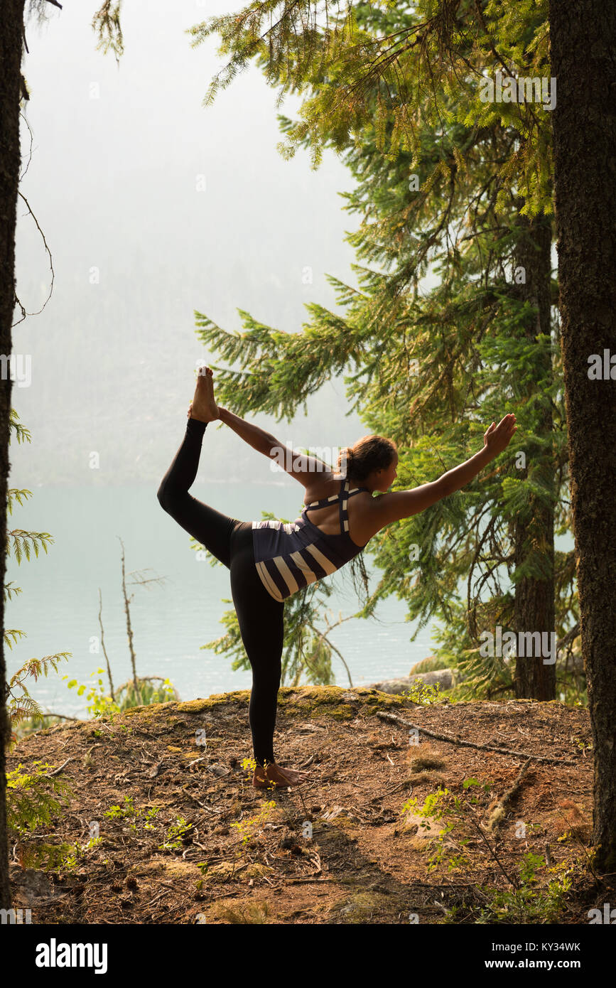 Colocar mujer realizar ejercicio de estiramiento en un exuberante bosque verde Foto de stock
