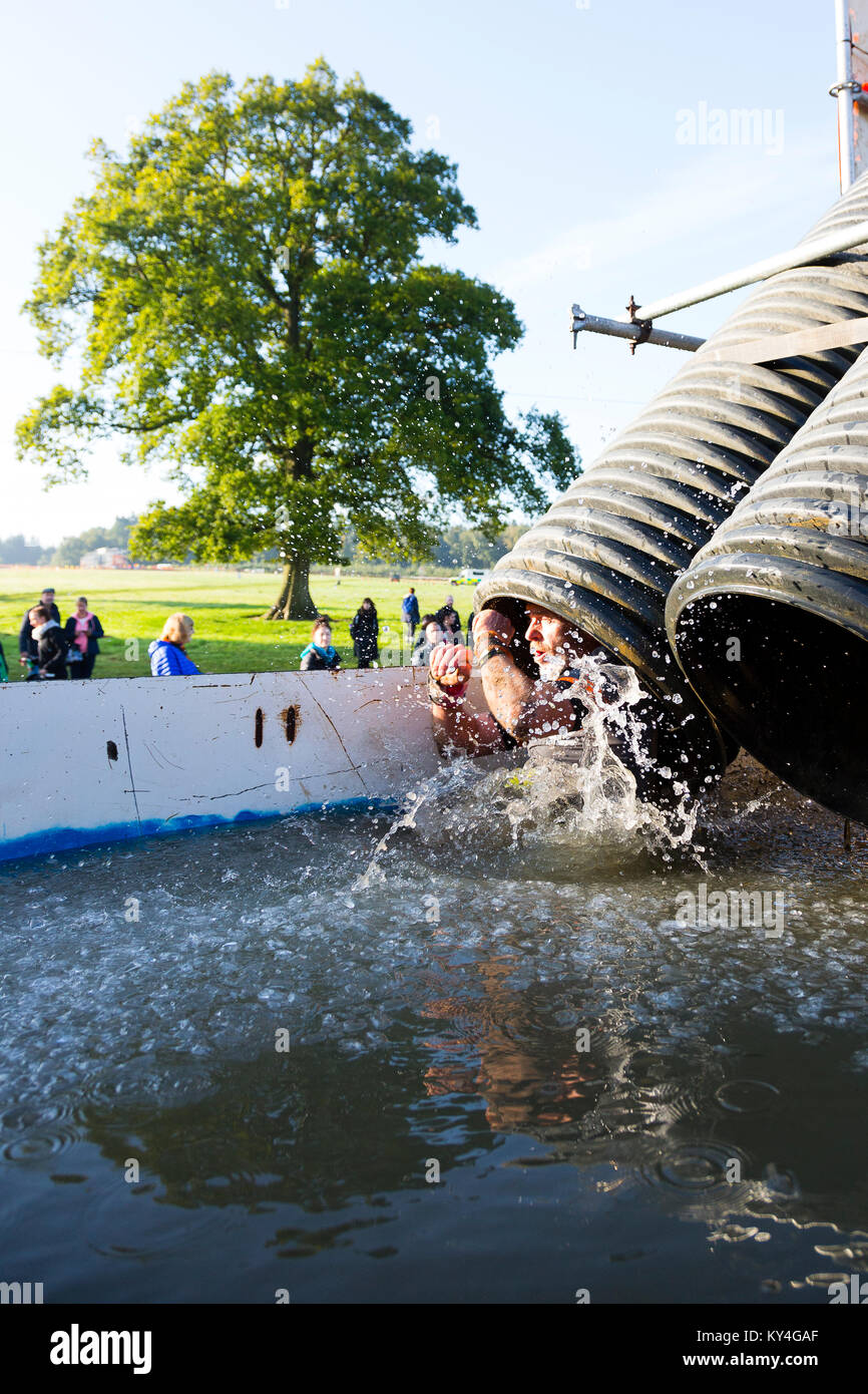Sussex, Reino Unido. Un competidor masculino ha salpicado el "Arctic Enema' obstáculo - una helada piscina de agua helada - durante una dura Mudder evento. Foto de stock