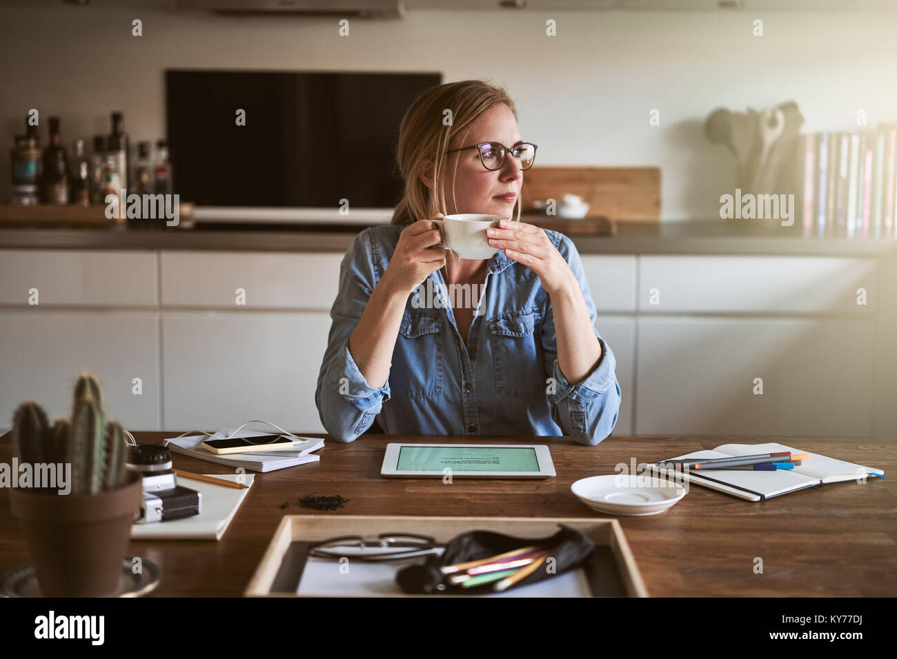 Joven empresario mirando a través de una ventana mientras bebe café y en una mesa de trabajo en su cocina Foto de stock