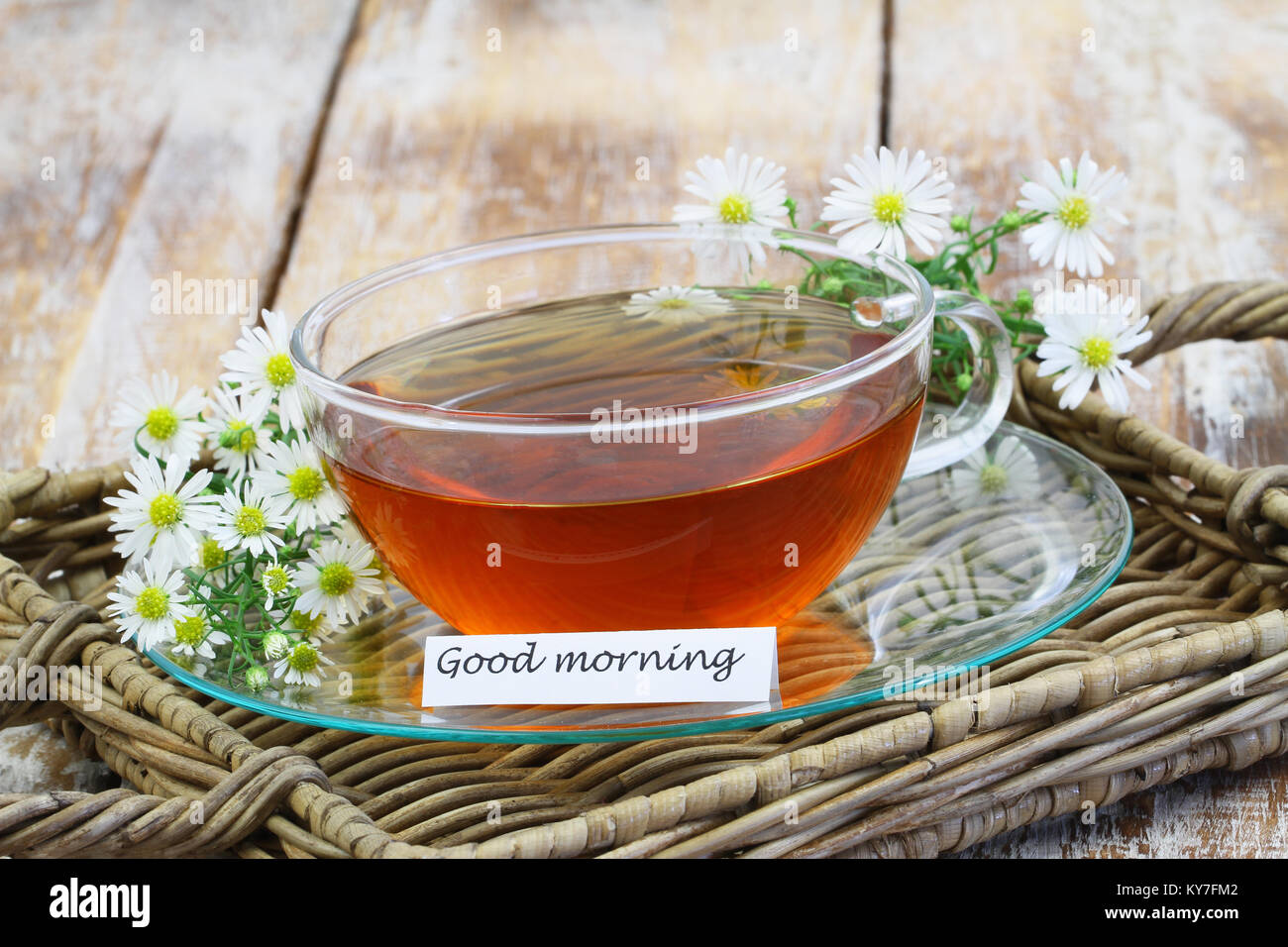 Tarjeta de buena mañana con un té de manzanilla en la taza transparente con frescas flores de