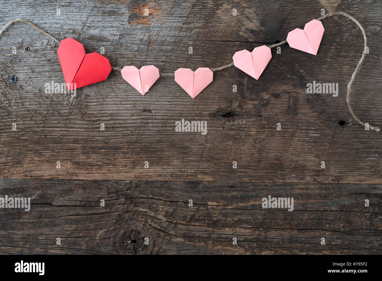 Origami corazones de papel en rojo y rosa para el Día de San Valentín  dispuestos en cadena contra rústico, madera desgastada antecedentes  Fotografía de stock - Alamy