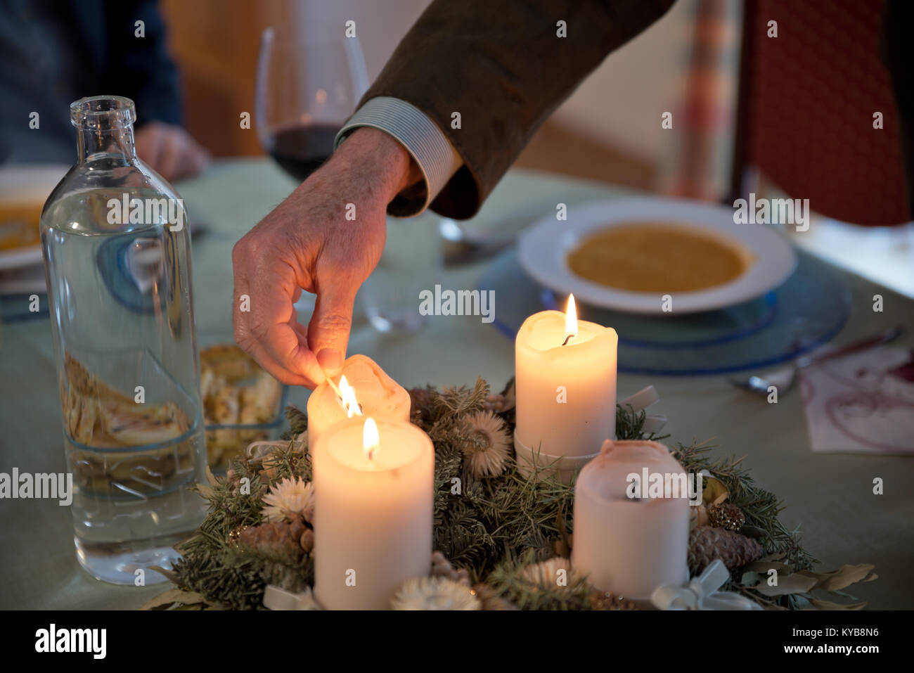 hipoteca Antagonista eje Persona de encender las velas en una corona de adviento ricamente decorado  con un partido en una mesa sentado solemnemente, listo para una cena de  Navidad Fotografía de stock - Alamy