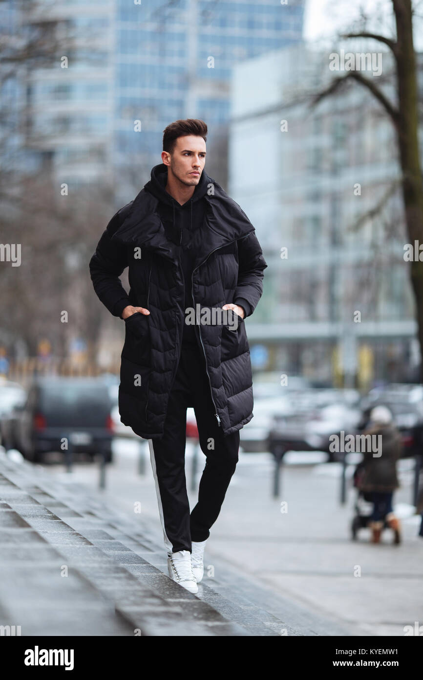 Hombre elegante wolk en la calle. El frío del invierno outfit. Gran  chaqueta con zapatillas blancas. Antecedentes Blured street. Foto modelo  profecional Fotografía de stock - Alamy