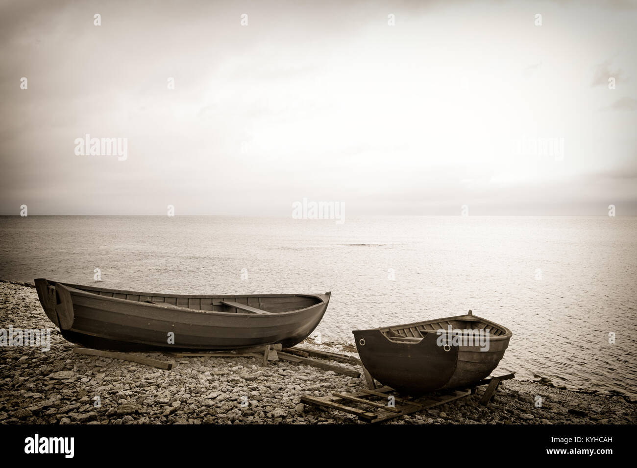 Dos botes de remos de madera en una playa rocosa al borde del mar. Imagen en tonos sepia moody de ensueño. Copie el espacio. Ubicación: Isla Faro, Suecia Foto de stock