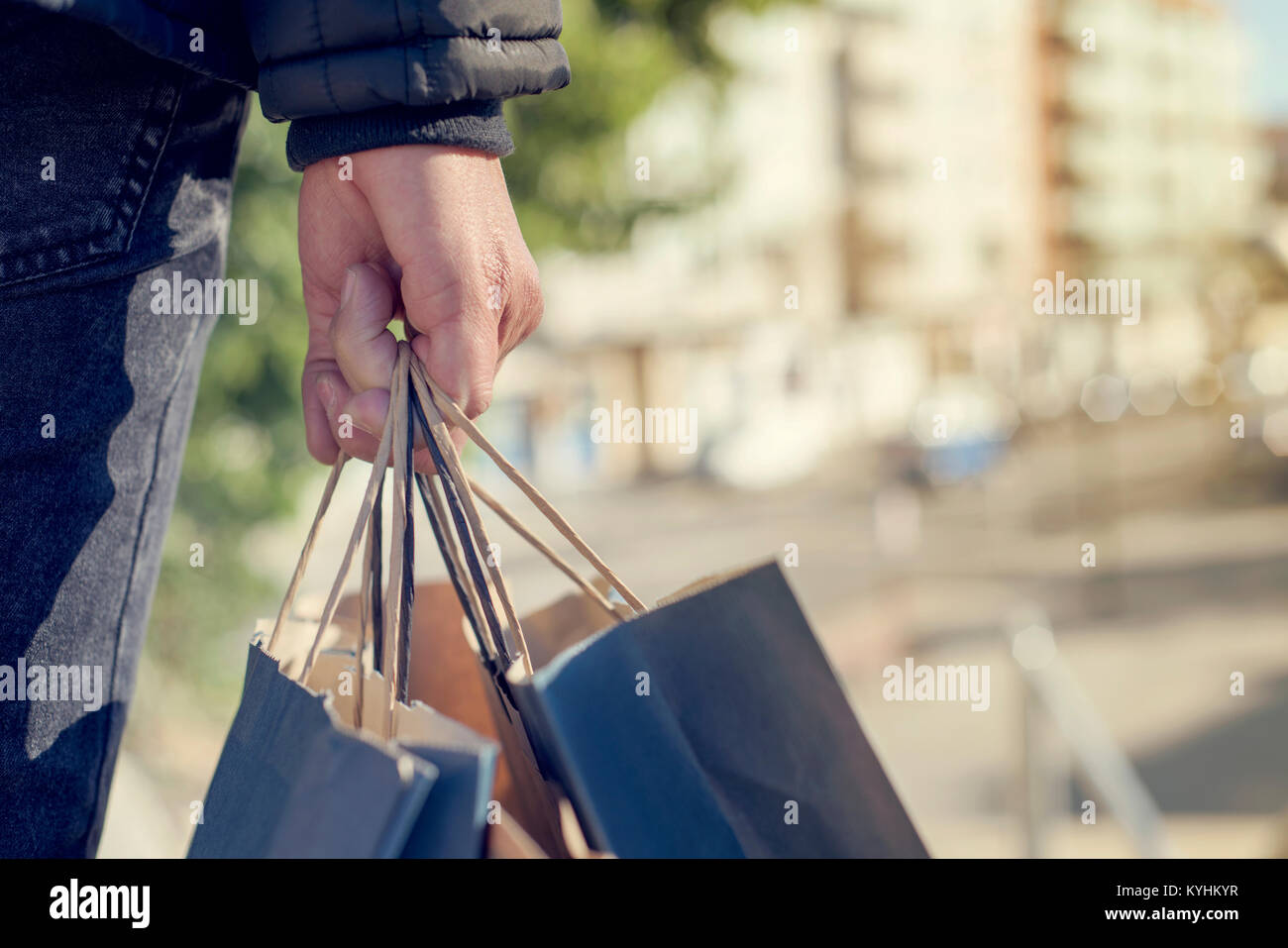 Primer plano de un joven hombre caucásico visto desde detrás de llevar algunas bolsas de papel con sus compras en la calle Foto de stock