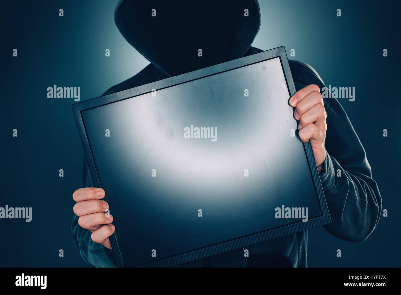 La ciberseguridad, hacker sosteniendo en blanco la pantalla del monitor del ordenador con hoodie y oscurecida cara Foto de stock