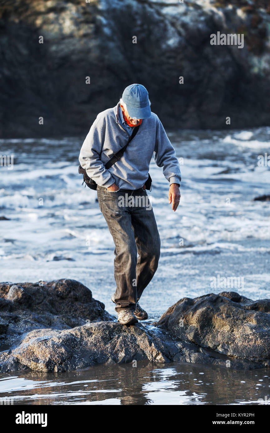 Equilibrio hombre senior en rocas mientras senderismo en la playa. Actividades físicas al aire libre promueve el envejecimiento saludable, la coordinación, el equilibrio y la confianza. Foto de stock