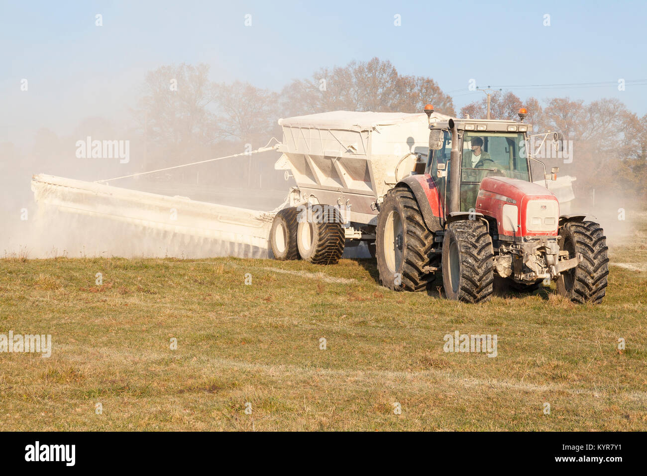 Agricultor usando un Massey Ferguson 8240 tractor y esparcidor para producto químico la fertilización de praderas en otoño tardío al atardecer Foto de stock