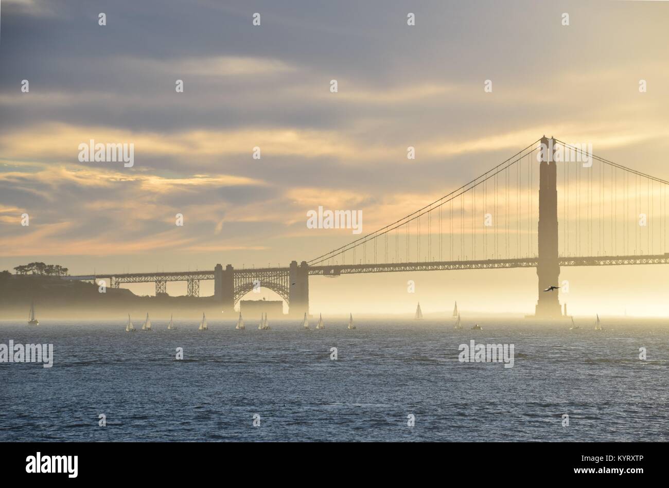 Una flotilla de pequeños barcos de vela al atardecer en el puente Golden Gate, San Francisco. Foto de stock