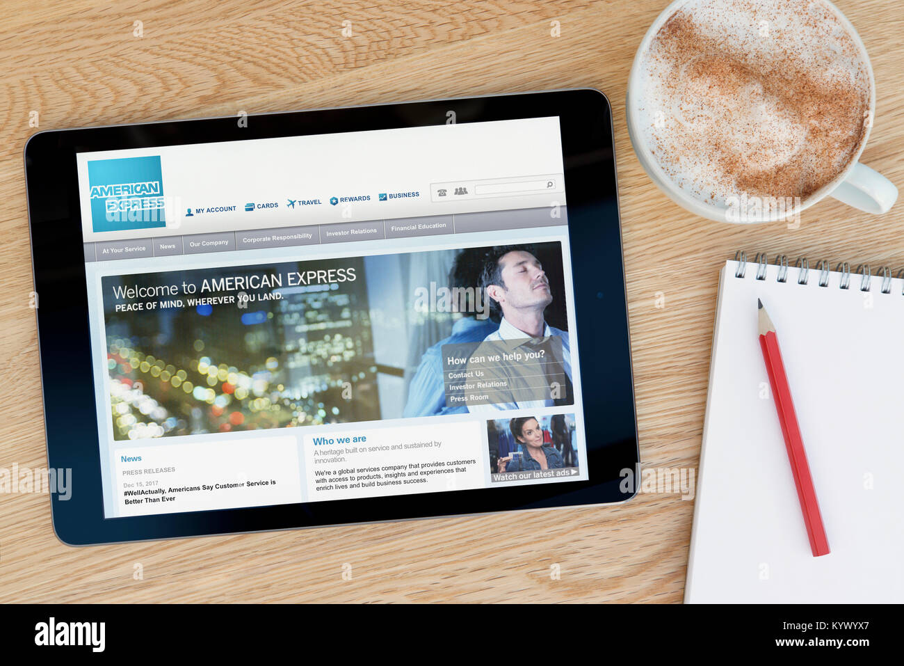 El sitio web de American Express en un iPad, en una mesa de madera junto a un bloc de notas, lápiz y la taza de café (Editorial) Foto de stock
