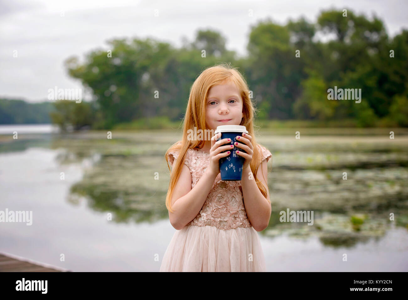 Retrato de Chica sujetando la copa desechable mientras está de pie contra el lago Foto de stock